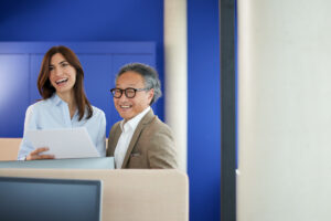 Zwei Kolleg:innen von Mitsui Chemicals Europe lächeln und halten Dokumente im modernen Büro.